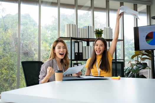 Asian smart Office or businesswoman excited successful business people, celebrating win. Two businesswoman looking at a monthly summary of sales that exceed sales targets and achieve profitable growth photo