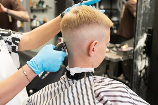 A boy is sitting in a barber shop, cutting his hair with a clipper photo