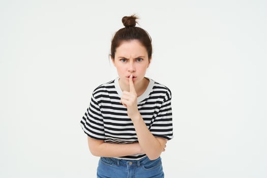 Image of angry woman shushing, makes hush gesture, press finger to lips with frustrated face, keep quiet, scolding loud person, white background photo
