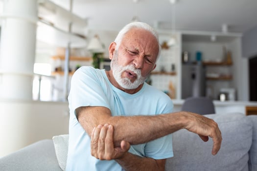 Senior man with arm pain.Old male massaging painful hand indoors. Old man hand holding his elbow suffering from elbow pain. Senior man suffering from pain in hand at home. Old age, health photo
