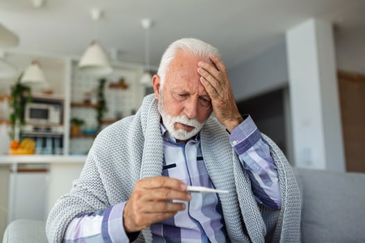 Sick elderly man checking his temperature suffering from seasonal flu or cold lying on sofa caughing suffering from seasonal flu or cold. . Ill senior feel unhealthy with influenza at home photo