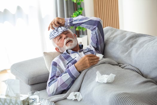 Mature man feeling sick with cold and fever at home, ill with flu disease sitting on the sofa with ice pack on his head photo