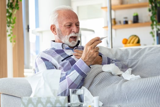 Sick elderly man checking his temperature suffering from seasonal flu or cold lying on sofa caughing suffering from seasonal flu or cold. . Ill senior feel unhealthy with influenza at home photo