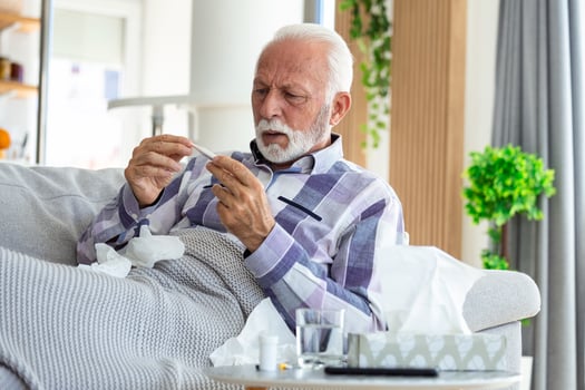 Sick elderly man checking his temperature suffering from seasonal flu or cold lying on sofa caughing suffering from seasonal flu or cold. . Ill senior feel unhealthy with influenza at home photo