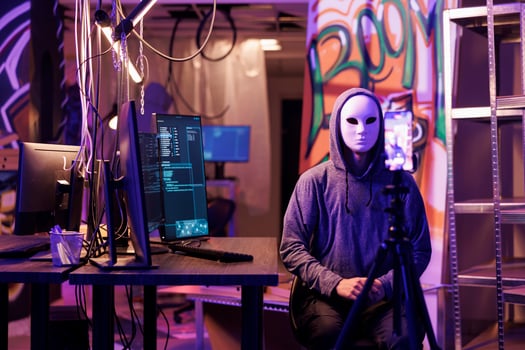 Anonymous hacker recording threat video with ransom message on smartphone to steal privacy information. Internet criminal calling victim using mobile phone in abandoned warehouse photo