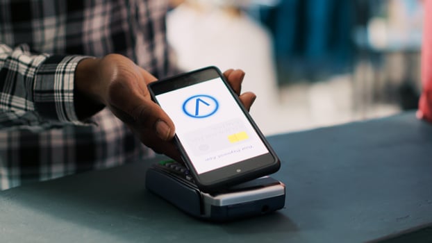 African american man putting mobile phone on pos terminal paying for fashionable clothes in boutique after discussing items material with worker. Man standing at retail store counter in clothing store photo