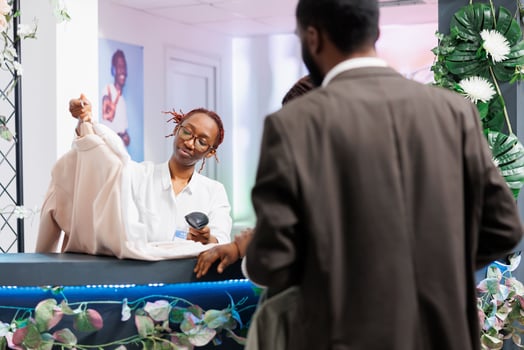 Clothing store cashier taking apparel from buyer and scanning barcode at checkout counter. Customers standing in queue while shopping mall employee using pos scanner at cash register photo