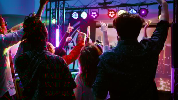 Cheerful adults having fun with DJ music on panel station, dancing under disco lights on dance floor. Young crowd of friends partying and clubbing with modern funky beats. Handheld shot. photo