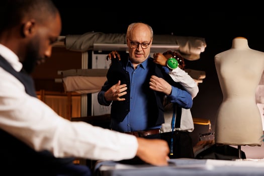 Senior customer trying on bespoke custom elegant suit vest before important business meeting. Elderly businessman checking out handmade fitting sartorial garment helped by experienced seamstress photo