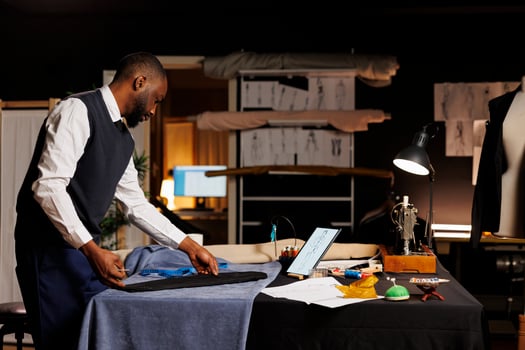 Expert suitmaker stiching together bespoken business suit, looking online for inspiration. Skilled couturier working in professional atelier shop, creating premium quality custom made clothing piece photo