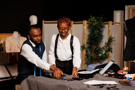 Precise suitmaking process in tailoring studio by african american fashion designers cutting sartorial textile material before making handmade costume. Couturiers working on customer comission photo