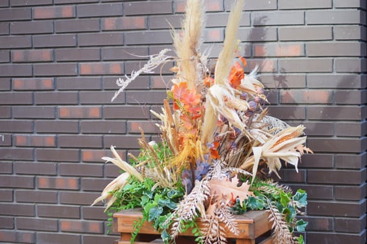 Autumn street decor, composition of dried flowers, leaves and heads of grass and cereals on the background of a brick wall. photo