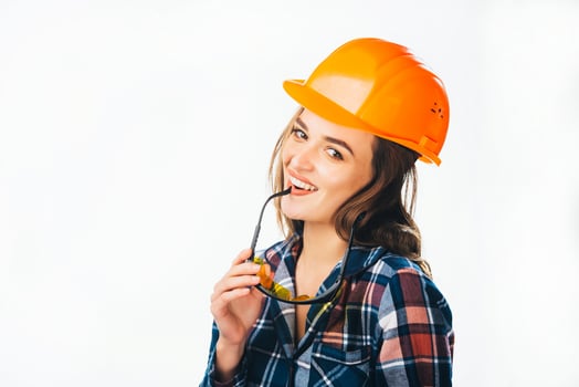 Portrait of passionate female builder with helmet and glasses touching her lips looking at camera and smiling. Sexy woman in protective helmet, glasses holding in hand. photo