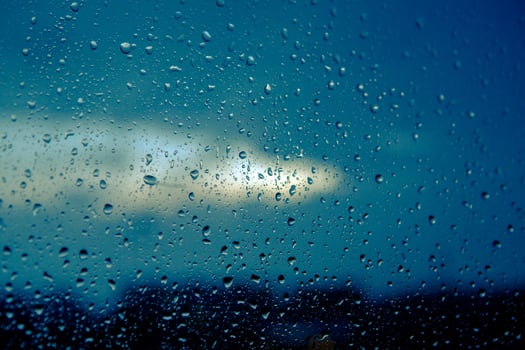 Water drops on glass against blue cloudy sky in the evening. Drops of rain on window in the dark background. Close-up. photo