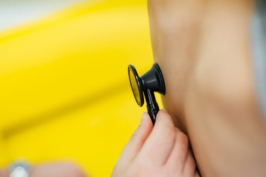 Close-up af naked body with a stephoscope. Unrecognizable hand holding stethoscope and listening kid's back on the yellow background. Close-up photo