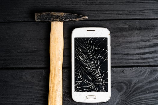 Smartphone smashed by hammer isolated on black wooden background. Broken touchscreen of a smartphone lying close to the hammer on table. photo
