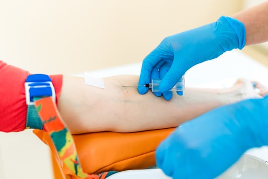 Nurse is pricking needle for the syringe into the patient's arm to take blood sample in a lab. Woman's hands in protective blue gloves makes an injection into a vein. Close-up. photo