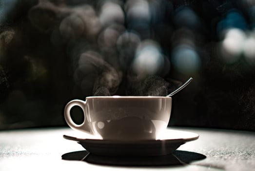 White cup with hot liquid and steam on black blurred background. Teaspoon in a cup. Tea and coffee concept. photo