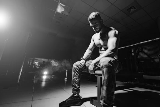 Man rests in gym after having a workout. Storng male with perfect body in the dark background with smoke. Closeup. photo