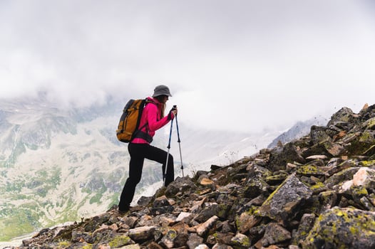 woman traveler goes to the top of the mountain. A girl with trekking poles and a backpack stopped to admire the fog approaching her in the mountains photo