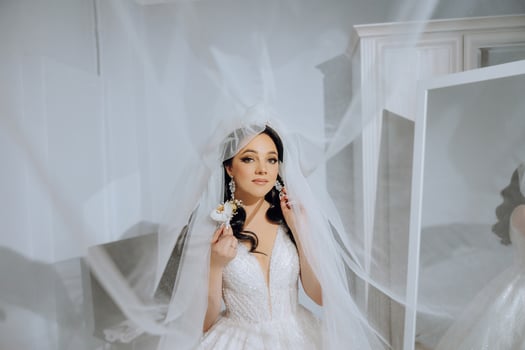 Beautiful young bride holding veil in white wedding dress, portrait of brunette bride in hotel room, morning before wedding. photo
