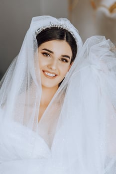 fashion photo of a beautiful bride with dark hair in an elegant wedding dress and stunning makeup in the room on the morning of the wedding. The bride is preparing for the wedding