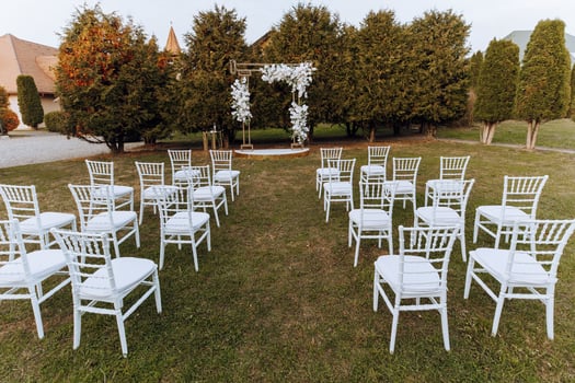 Decor at the wedding. Many white chairs and a golden arch decorated with white flowers photo
