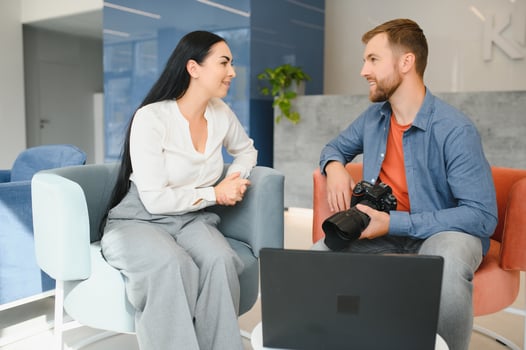 Young photographer man in blue shirt watching photo with client woman after photo session and smiling and looking at each other