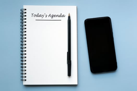 TODAY'S AGENDA written on notebook with pen and smartphone on blue background. photo