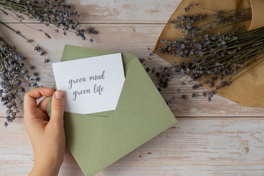 Female hands taking paper card note with text GREEN MIND GREEN LIFE from envelope. Lavender flower. Top view, flat lay. Concept of eco sustainability lifestyle mental spiritual health self care photo