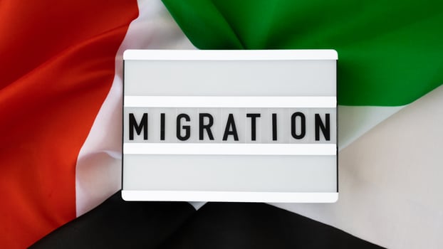 Message MIGRATION on background of UAE flag made from silk. United Arab Emirates national flag with concept of tourism and traveling. Dubai welcoming card. Advertisement photo