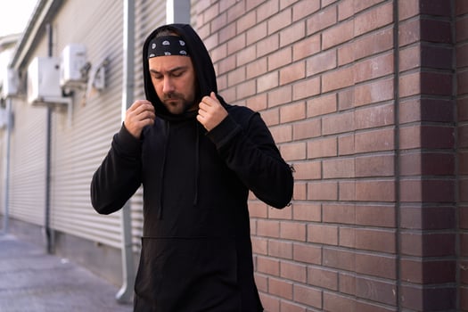 Handsome young unshaven man black hoodie and bandana stands backyard near brick walls summer day. photo