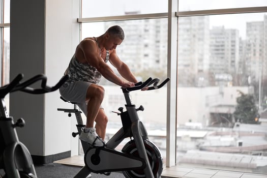 Muscular athletic bodybuilder fitness model sitting stationary bicycle in gym near big window photo