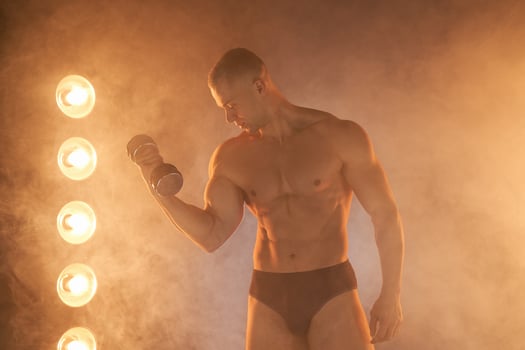 Young athlete pumping dumbbells, practicing biceps training, smoky illuminated background photo