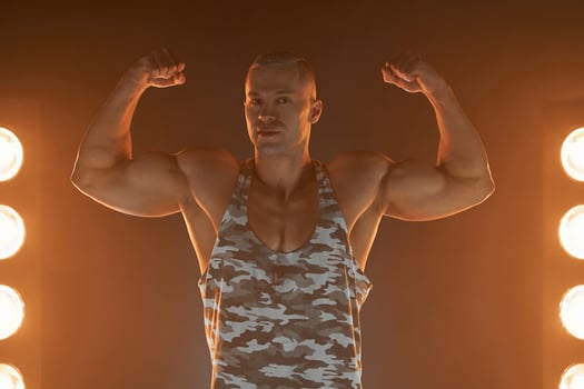 Active lifestyle. Professional bodybuilder showing biceps and smiling at camera, lamps illumination on background photo