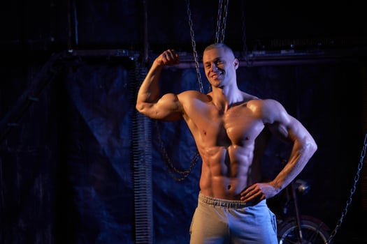 Young shirtless muscular man standing among metal chains, looking at camera, copy space photo
