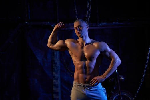 Young shirtless muscular man standing among metal chains, looking at camera, copy space photo