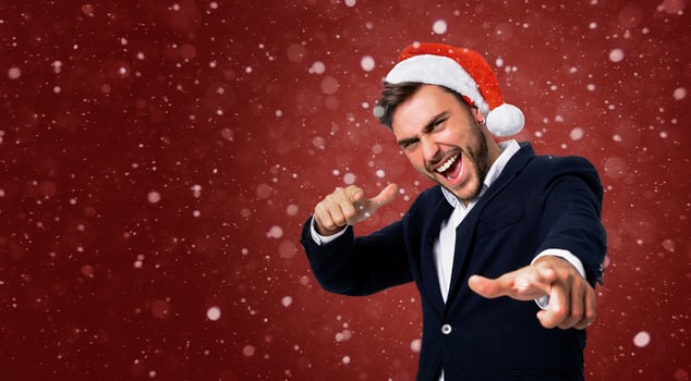 Young handsome caucasian guy in business suit and Santa hats stands on red background in studio smilie and showing Finger to the camera. photo