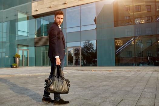 Men's fashion. A young male businessman in a trendy suit and a white shirt with a big black handbag comes out from a fashionable clothing store. photo