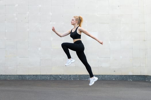 Sport and Fitness Concept Young Adult Caucasian Female Athlete Jumping High Outdoor Gray Tail Wall Background photo