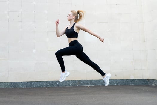 Sport and Fitness Concept Young Adult Caucasian Female Athlete Jumping High Outdoor Gray Tail Wall Background photo