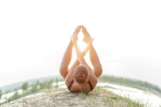 A beautiful Caucasian girl in a black swimsuit do yoga position on nature against the backdrop of the bright sun. photo