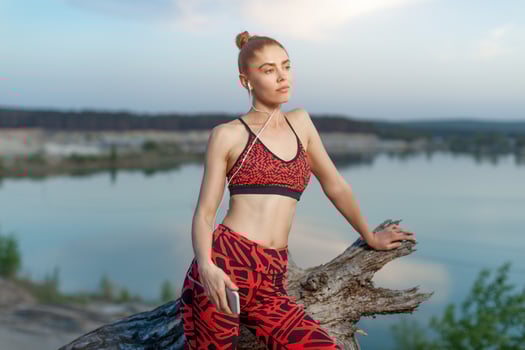 A beautiful brunette girl in stylish sports clothes is resting after a sport active workout near the lake. photo