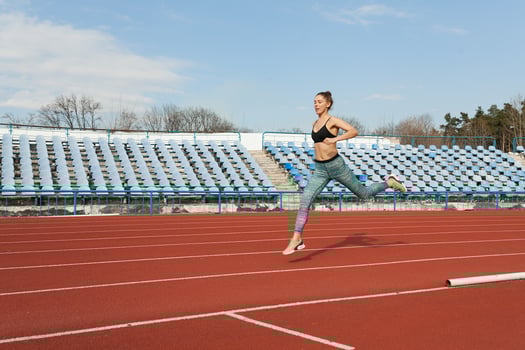 Young woman running during sunny morning on stadium track photo