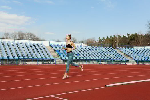 Young woman running during sunny morning on stadium track photo