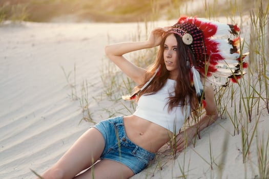 A beautiful young Caucasian girl in a white top on her head is wearing an Indian hat. Roach is in the desert. Happy holiday mood. photo