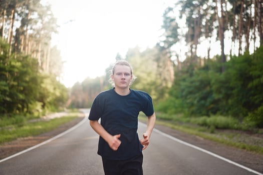 Caucasian young curly man athlete runs sunny summer day on asphalt road in the forest. photo