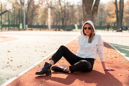 Outdoor portrait of young beautiful woman with long in sunglasses and a white hooded sweater sitting on the sportsground track photo