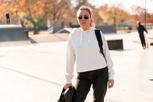 Outdoor portrait of young beautiful woman with a ponytail and sunglasses, with a backpack on his shoulders, dressed in a white sweater, near the sportsground photo