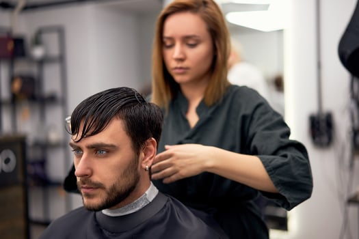 Handsome blue eyed man sitting in barber shop. Hairstylist Hairdresser Woman cutting his hair. Female barber. photo